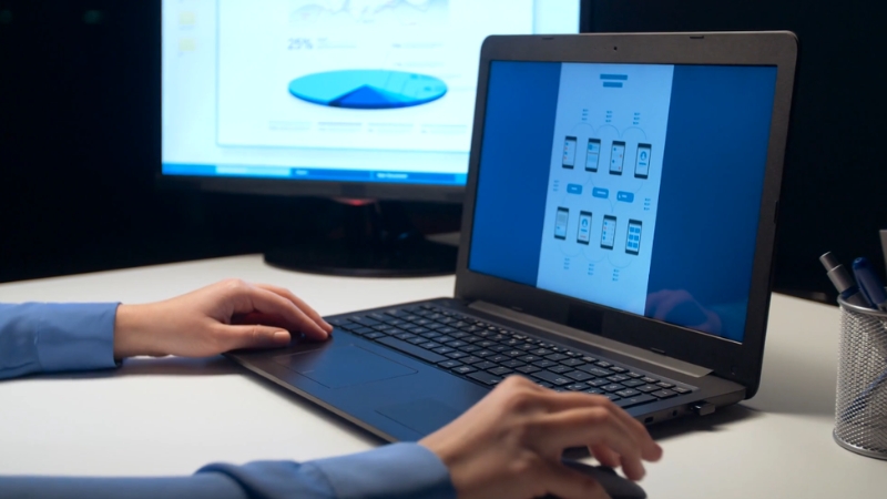 A designer working on a UI/UX design project on a laptop with data visualizations in the background
