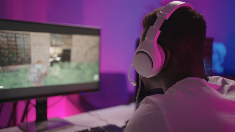 A gamer wearing white headphones plays on a PC, showing how UX design affects the ease of navigating video games