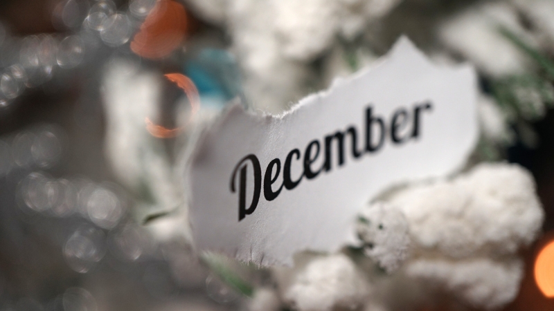 A torn paper with December written on it rests on snowy holiday decorations