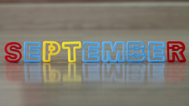 Colorful plastic letters spelling September sit on a wooden surface with reflections