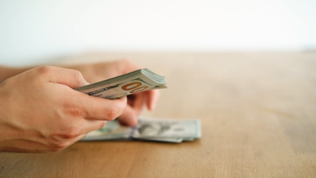 Hands counting dollar bills, symbolizing budget and media planning tips for YouTube in modern B2B marketing