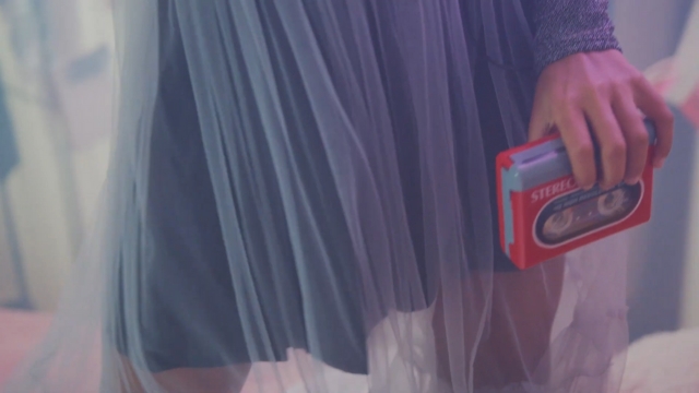 A person holds a retro cassette player while wearing a sheer skirt, highlighting vintage style in a modern setting