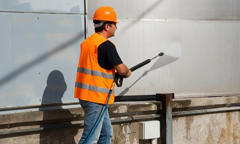 A man in an orange vest is operating a pressure washer
