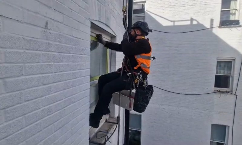 A man in an orange vest is climbing up the side of a building