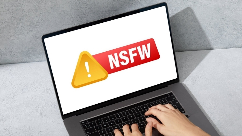 Hands using a laptop that shows an NSFW warning icon related to region-based content restrictions