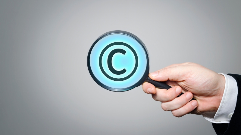 Hand holds a magnifying glass over a copyright symbol during a copyright infringement investigation