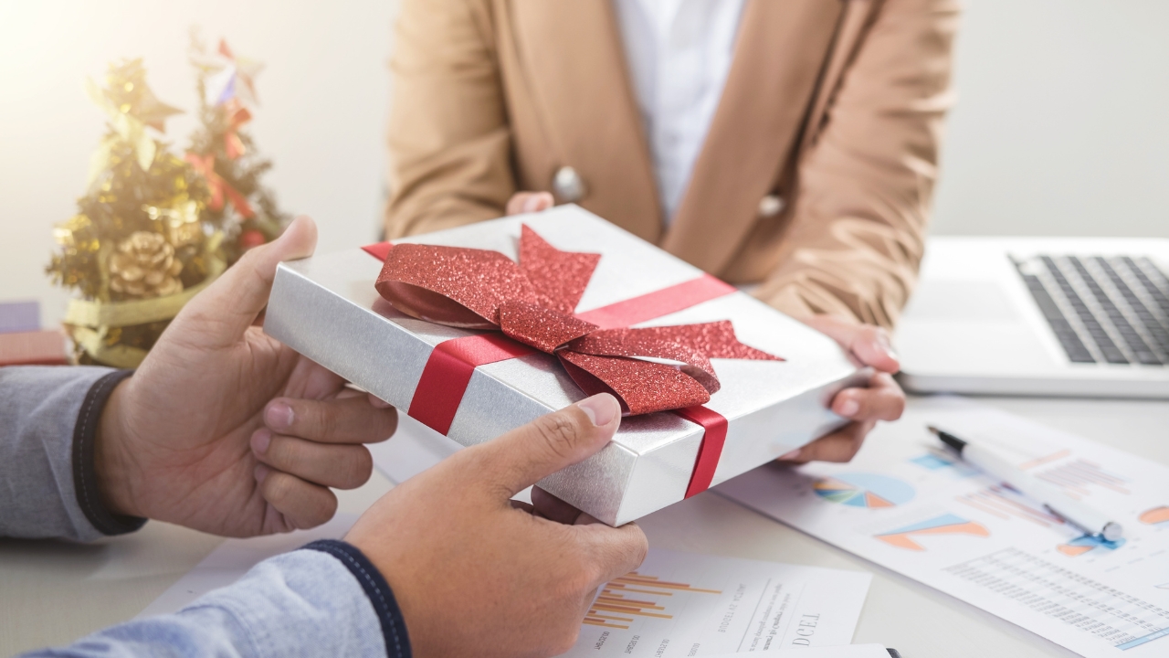 Hands exchange a wrapped corporate gift across an office desk