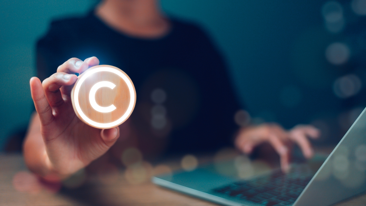 Person holding a glowing copyright symbol in front of a laptop to illustrate copyright rules for online content