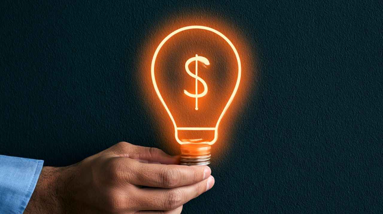 Hand holding a glowing light bulb with a dollar sign.